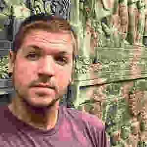 Timm, author, creator and travel blogger of Llama Socks Travel Guide posing for a selfie at some ancient ruins in Cambodia. He is a solo gay male traveler.