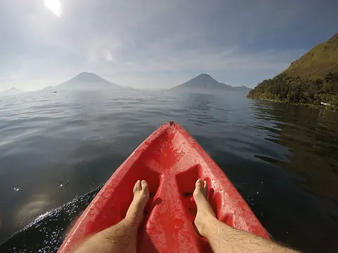 a mans feet while kayaking on Lake Atitlan with volcan fuego in the distance