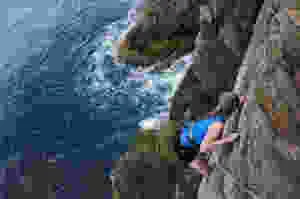 a female solo traveler takes a photo while climbing a cliff over the ocean