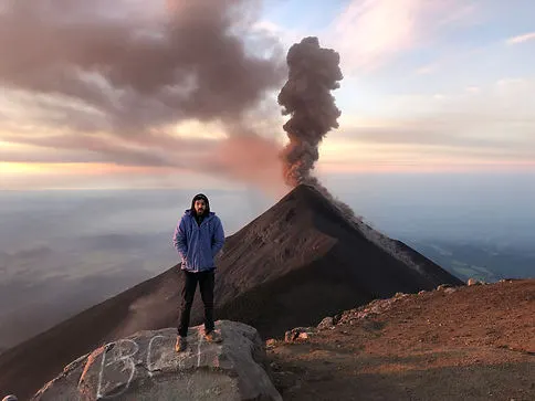a man posing next to volcan fuego on the acatenango volcano hike near Antigua Guatemala during sunrise