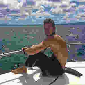 Timm, author, creator and travel blogger of Llama Socks Travel in a wetsuit on a boat before scuba diving underwater. He is a solo gay male traveler