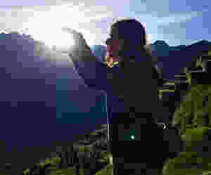 a female solo traveler poses for a picture in machu picchu where she uses forced perspective to look like shes holding the sun