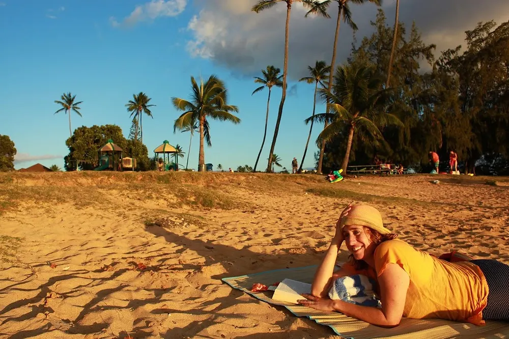 Meredith from Beautiful Voyager posing for a picture on the beach in Kauai Hawaii with palm trees and beautiful sand