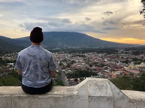a man sitting at the mirador viewpoint overlooking Antigua Guatemala and Volcan Fuego during sunset